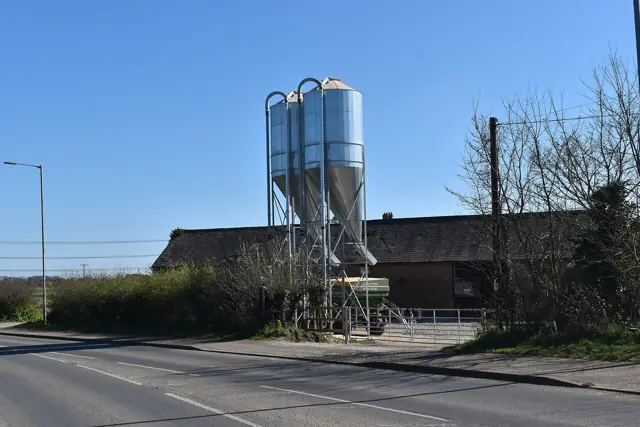 Two metal feed silos beside farm buildings