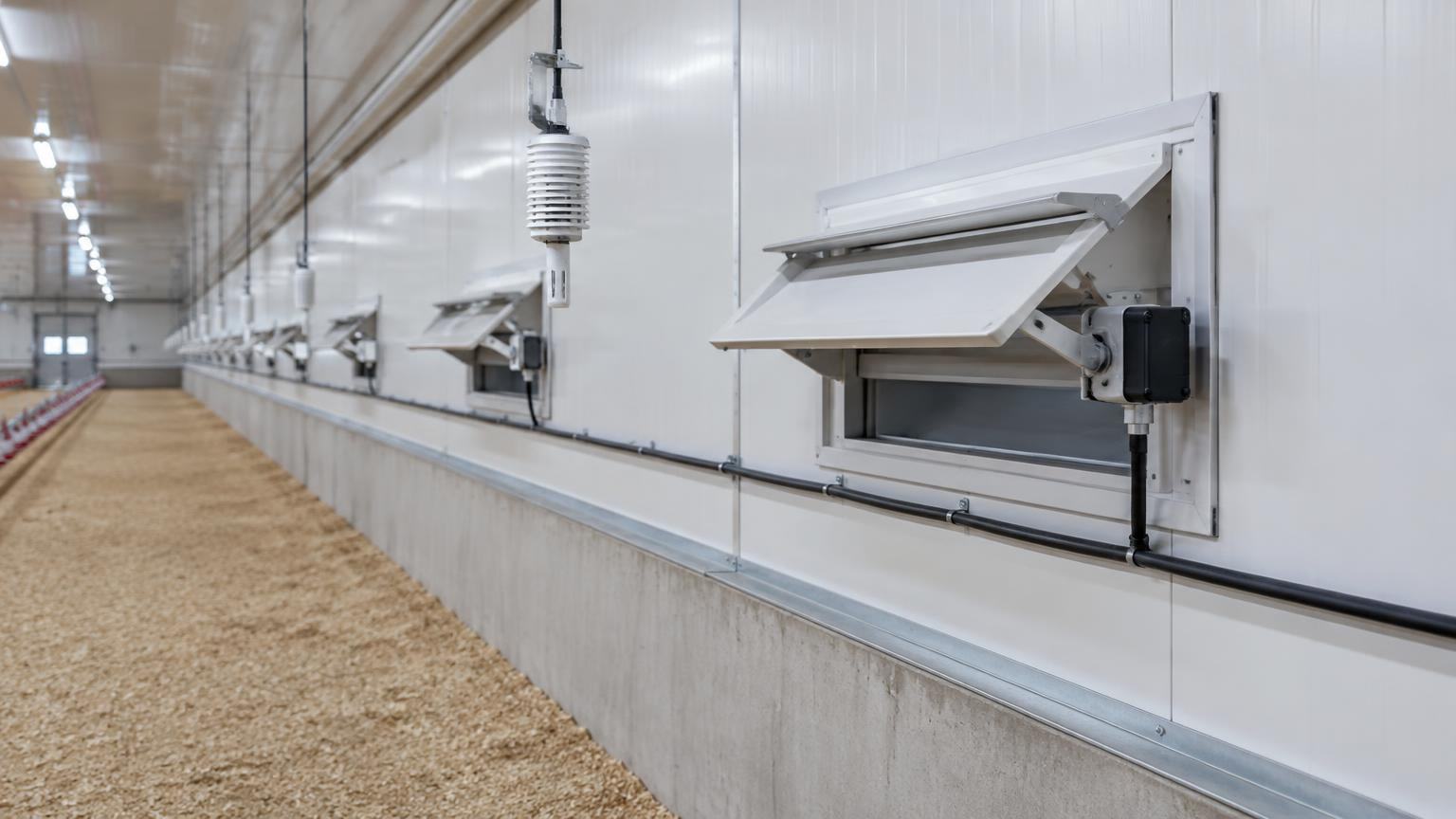 Row of motorised sidewall air inlets and a climate sensor in an insulated poultry house